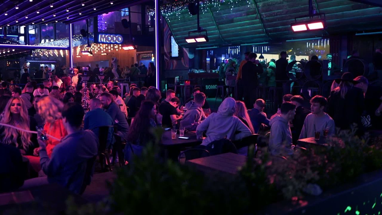 A packed SOHO terrace after dark under neon and fairy lights